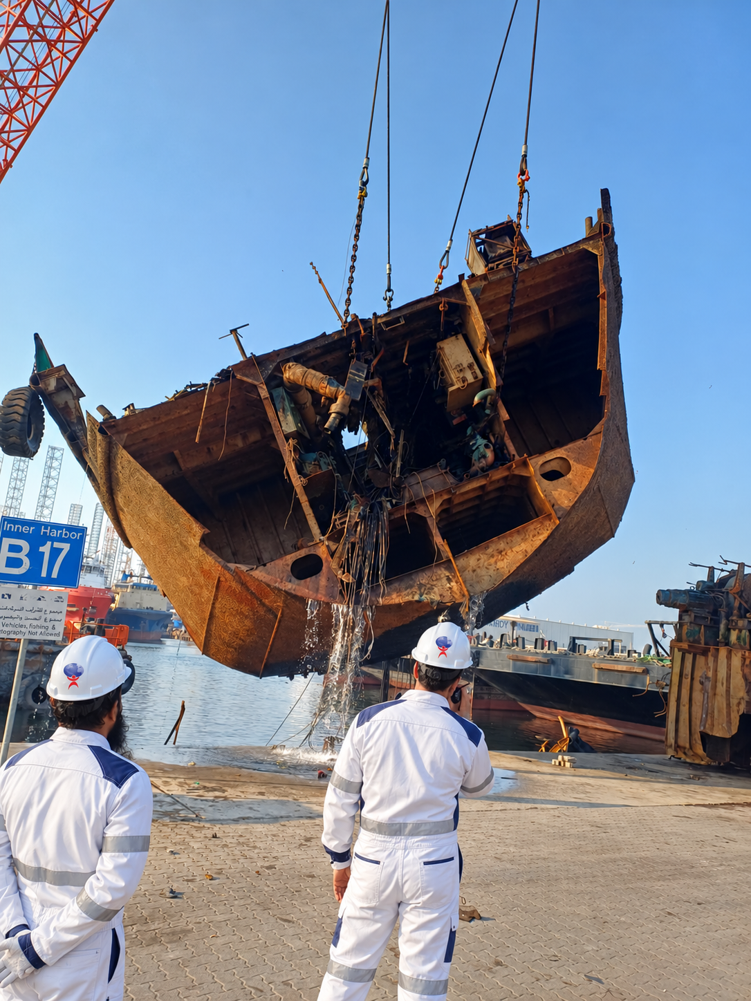 Fourteen Universe team in white PPE observing a lifted wreck at Hamriya Port